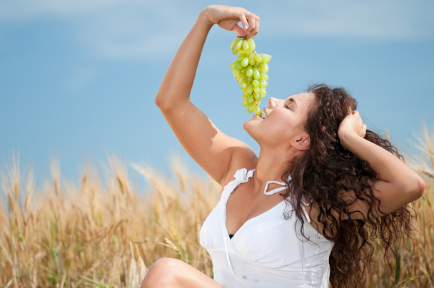 Perfect woman eating grapes in wheat field. Picnic. - Valokuva, kuva
