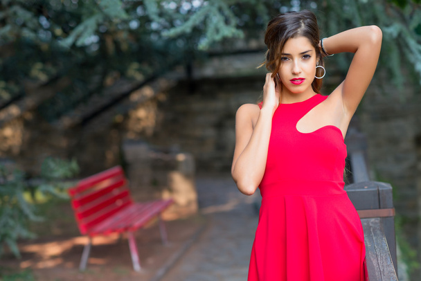Красивая девушка с красным платьем держа волосы руками
 - Фото, изображение