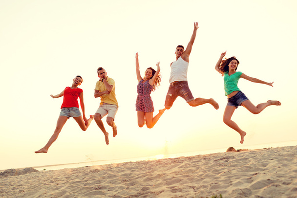 Lächelnde Freunde tanzen und springen am Strand - Foto, Bild
