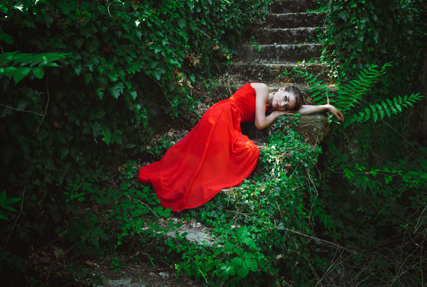 Mooie vrouw in de rode jurk liggend op de stappen van de oude trap - Foto, afbeelding