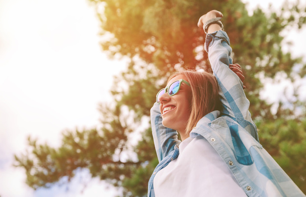 Woman with sunglasses raising her arms over nature background - Photo, Image