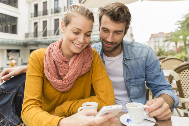 young couple using a smartphone at a bar terrace - Fotografie, Obrázek