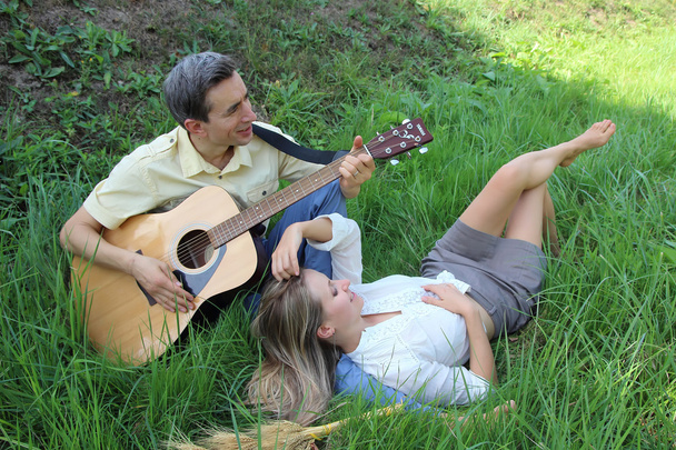 A young man plays the guitar for his girl in nature. - Zdjęcie, obraz