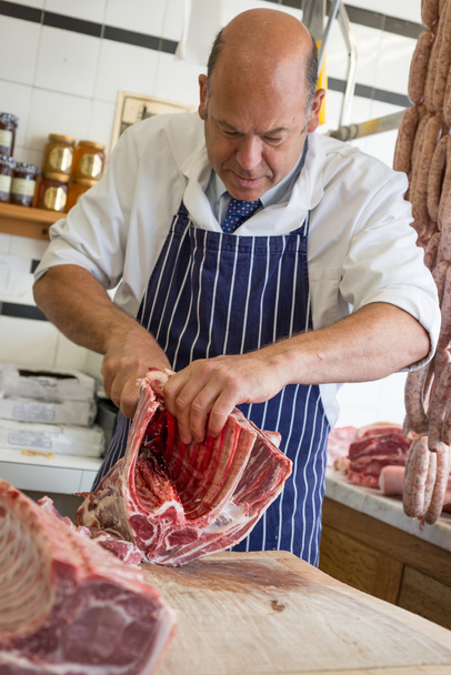 Butcher in shop butchering a rack of lamb with his hands - Photo, Image