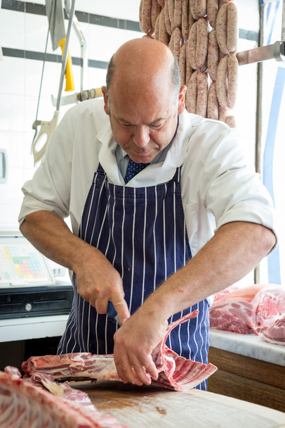 Carniceiro que corta a união de carne com uma faca afiada
 - Foto, Imagem