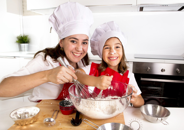 mère heureuse cuisson avec petite fille dans tablier et chapeau de cuisine avec pâte de farine à la cuisine
 - Photo, image
