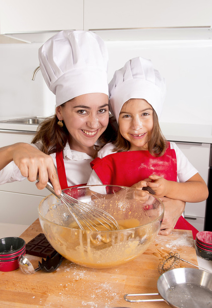 šťastná matka pečení s malou dcerou v zástěře a kuchař klobouk příprava těsta v kuchyni - Fotografie, Obrázek