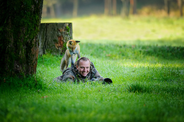 Naturfotograf versteckt im Gras mit neugierigem Fuchs auf dem Rücken - Foto, Bild