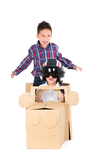 Adorable young boys playing and sitting in a cardboard car isolated over white background - Photo, Image