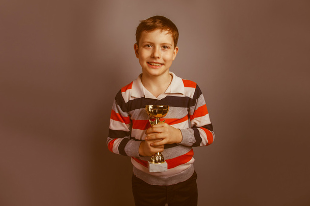 Europese uitziende jongen van tien jaar houden een kopje award op een grijs - Foto, afbeelding