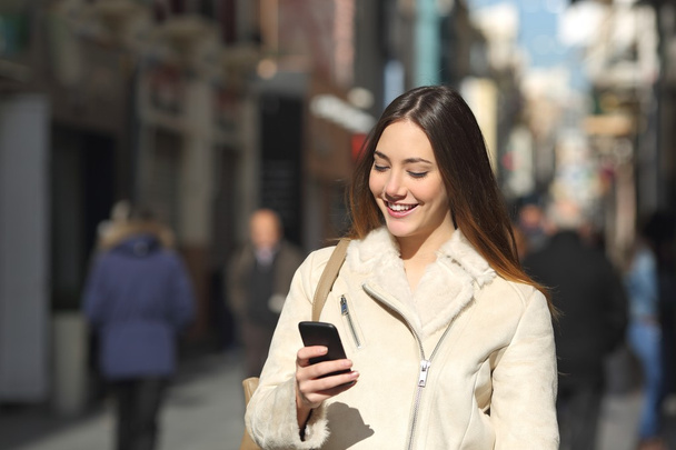 Meisje lopen en SMS op de slimme telefoon in de straat in de winter - Foto, afbeelding