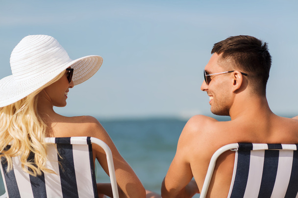 happy couple sunbathing in chairs on summer beach - 写真・画像