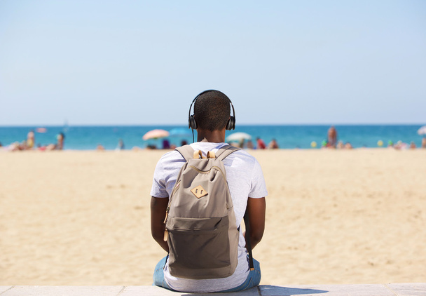 ヘッドフォンで音楽を聞いてビーチに腰掛けていた男 - 写真・画像