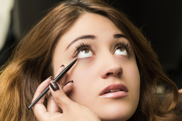 Closeup headshot brunette getting makeup treatment by professional stylist applying eyeliner - Photo, Image