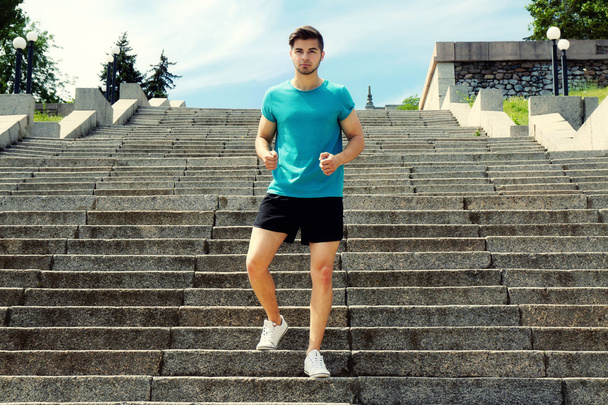 Young man jogging at stairs outdoors - 写真・画像