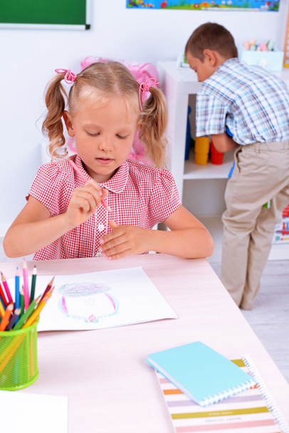 Little girl drawing at the desk in classroom - Фото, изображение