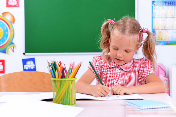Маленькая девочка рисует за столом в классе
 - Фото, изображение