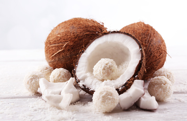 Bonbons en flocons de noix de coco et noix de coco fraîche sur fond bois clair
 - Photo, image