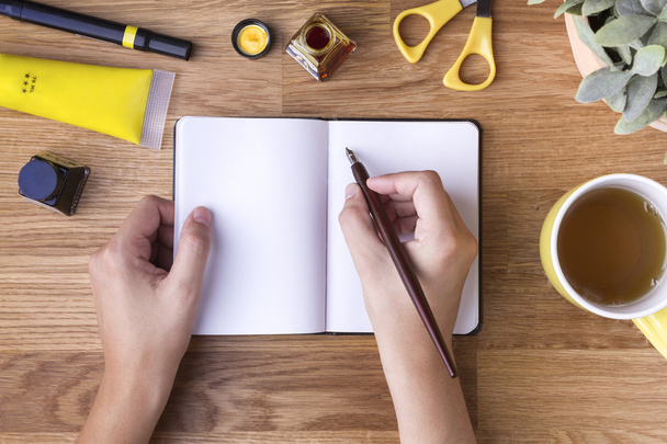 Hand met pen schrijven op lege Kladblok en gele objecten - Foto, afbeelding