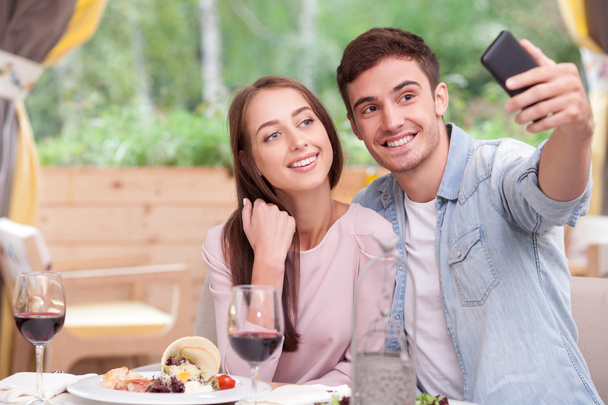 Attractive boyfriend and girlfriend are photographing themselves in cafe - Foto, Imagen