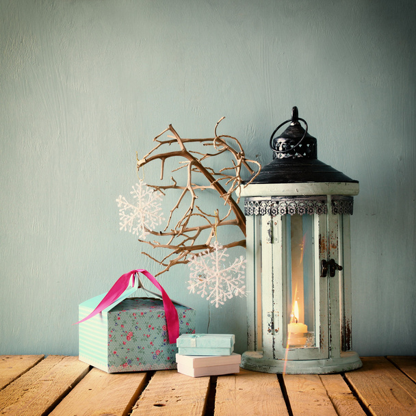 white wooden vintage lantern with burning candle christmas gifts and tree branches on wooden table. retro filtered. - Fotografie, Obrázek