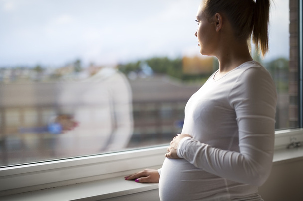 Продумана вагітна жінка дивиться у вікно
 - Фото, зображення