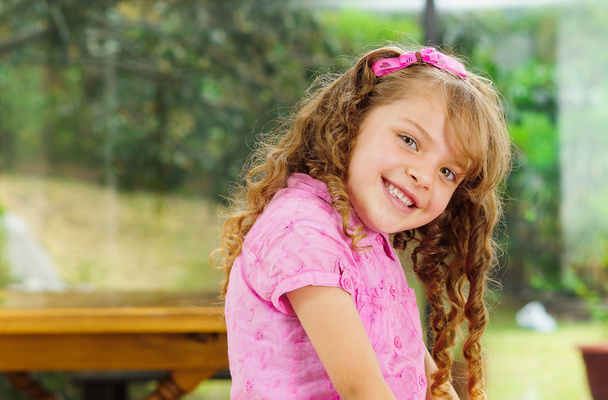 Beautiful young hispanic girl with pink clothing smiling cute at camera, blurry garden background - Fotoğraf, Görsel