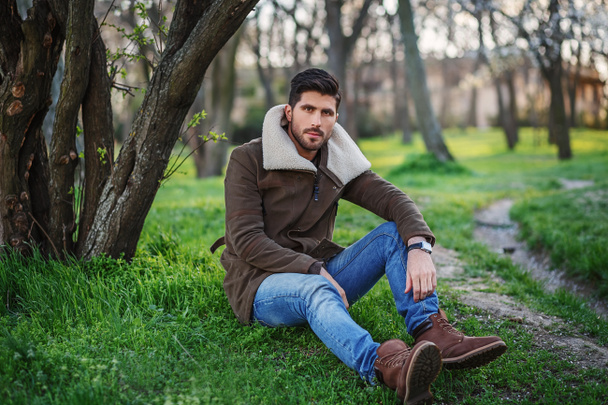 Портрет модного молодого привлекательного мужчины, сидящего на зеленой траве i
 - Фото, изображение
