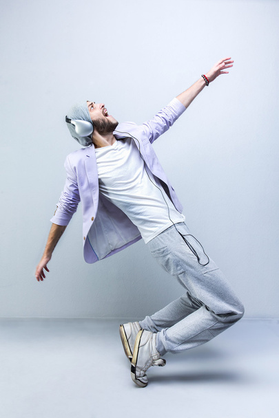 Handsome young stylish man in headphones dancing while standing against grey background. Full length. - Foto, afbeelding