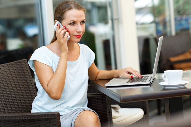 Mujer atractiva sentada en un café con una computadora portátil y hablando en
 - Foto, Imagen