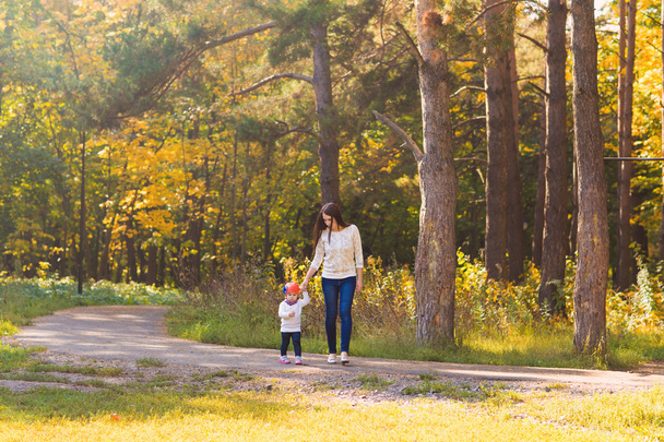 秋の公園で彼女の赤ちゃんを連れて歩いて若い母親 - 写真・画像