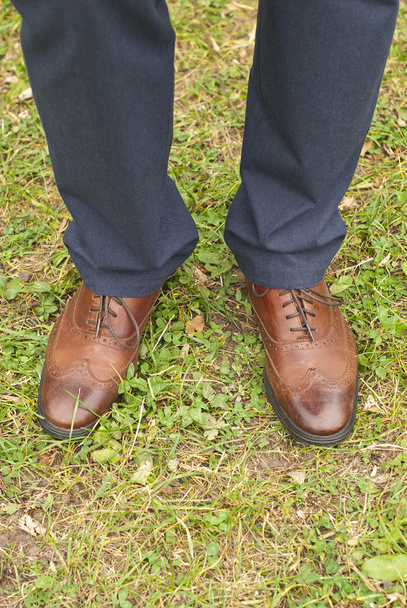Νέος μόδα στα πόδια του ανθρώπου σε μπλε τζιν και μπότες καφέ στο γρασίδι - Φωτογραφία, εικόνα