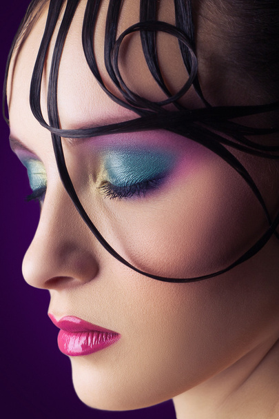 Young beautiful fashion model with pink and blue makeup and hairstyle on her face. purple background. studio shot. - Foto, immagini