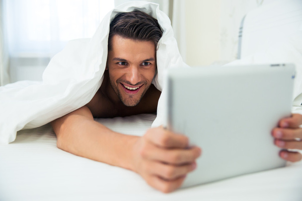 Man lying under blanket and using tablet computer - Foto, imagen
