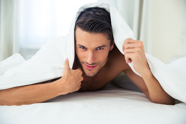 Handsome man lying under blanket in the bed - Valokuva, kuva