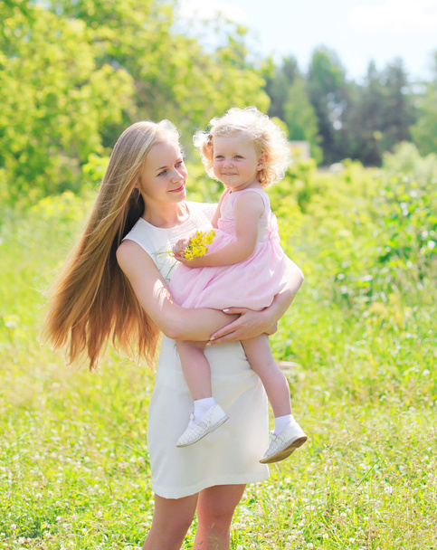 Hermosa madre sosteniendo en las manos del niño con flores en verano d
 - Foto, Imagen