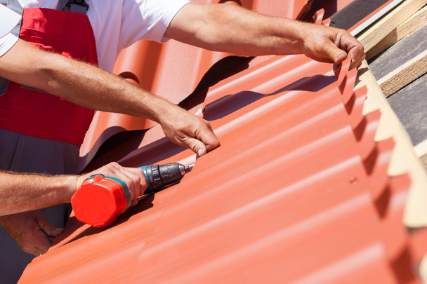 Εργαζομένων σε στέγη με ηλεκτρικό τρυπάνι εγκατάσταση κόκκινο μεταλλικό κεραμίδι στο ξύλινο σπίτι - Φωτογραφία, εικόνα