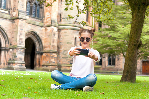 Nuori nainen istuu nurmikolla Glasgow 'n yliopiston puutarhassa
. - Valokuva, kuva
