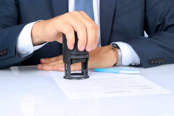 Primer plano de la mano del empresario presionando un sello en el documento en la oficina
 - Foto, imagen