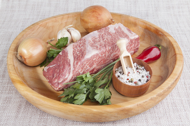A piece of fresh marbled beef, chili pepper, parsley, onion, garlic, ribs lie on a wooden tray - Fotó, kép