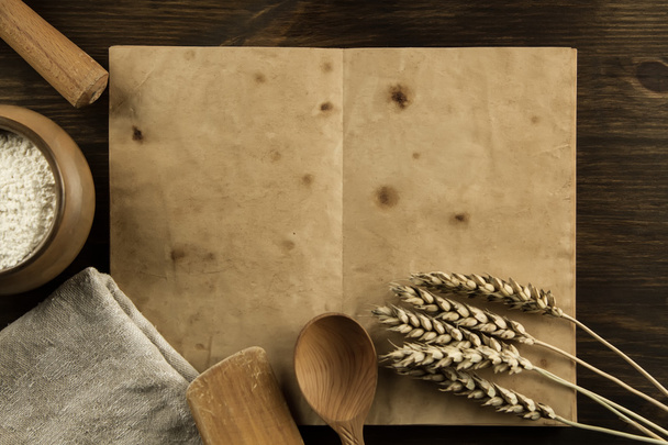 open old vintage book on the aged wooden background. Kitchen utensils, ears of wheat, flour in a pot. homemade, menu, recipe, mock up - Foto, imagen