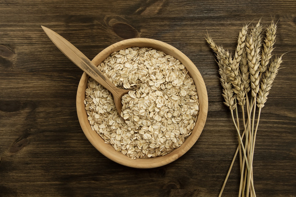 oatmeal flakes in a wooden bowl with a spoon, ears of wheat on the table. homemade, menu, recipe, mock up - Photo, image