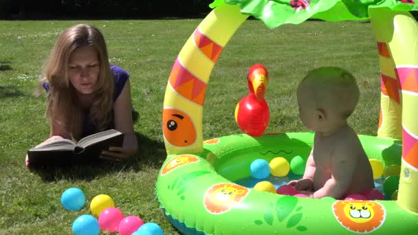 Mutter las Buch über Plaid und Baby im Kinderbecken. 4k - Filmmaterial, Video