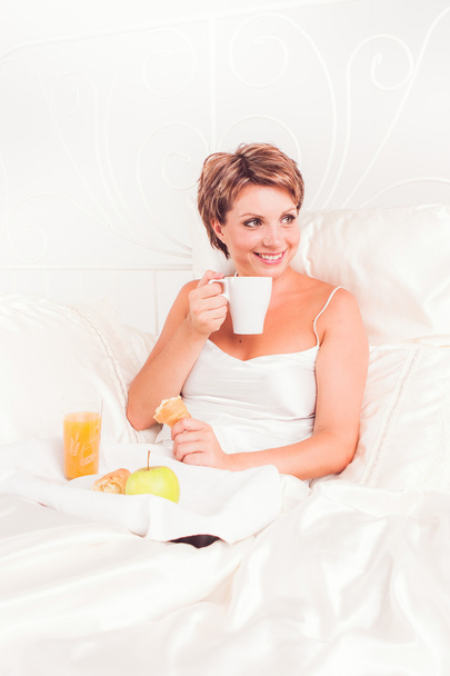 Lovely woman eating breakfast in her bed - Фото, изображение