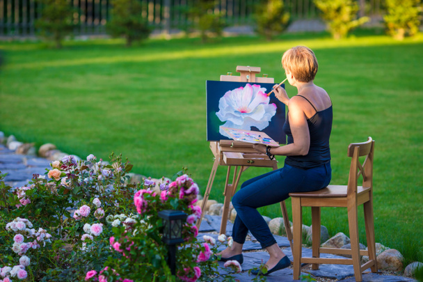 Femme heureuse peignant un tableau sur un chevalet par une journée chaude
 - Photo, image