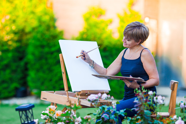 Счастливая женщина рисует картину на мольберте в теплый день
 - Фото, изображение