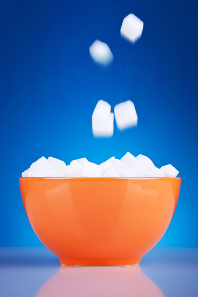 Кубики сахара падают в оранжевую миску
 - Фото, изображение
