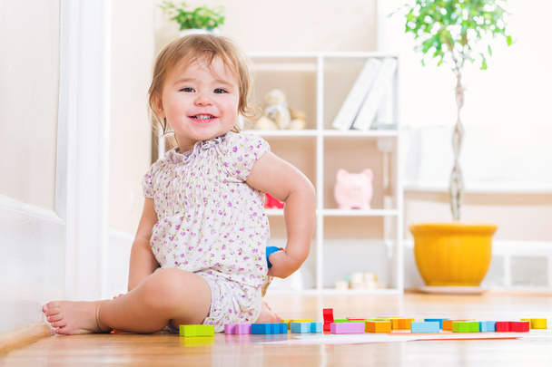 Toddler girl smiling while playing with wooden toy blocks - Zdjęcie, obraz