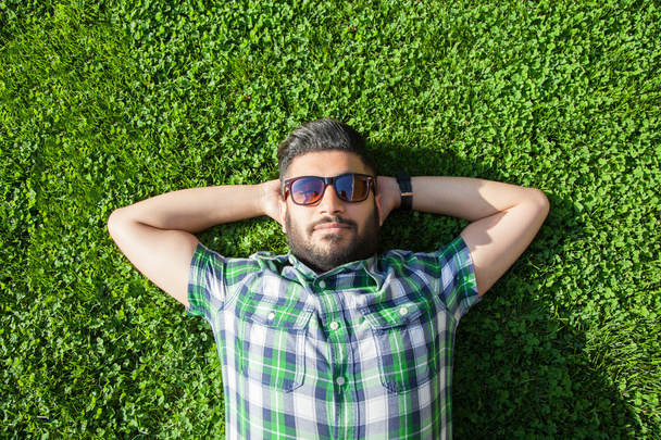 One fashion middle eastern man with beard, fashion hair style is resting on beautiful green grass day time. young arab businessman 20-30 years, resting after hard work. smart phone, tablet. - Foto, Imagem