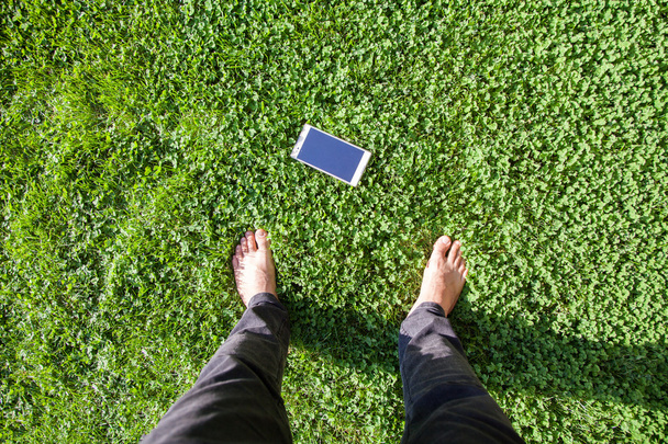 l'uomo trova il telefonino su erba. vista dall'alto del piede umano e del telefono cellulare sull'erba
. - Foto, immagini